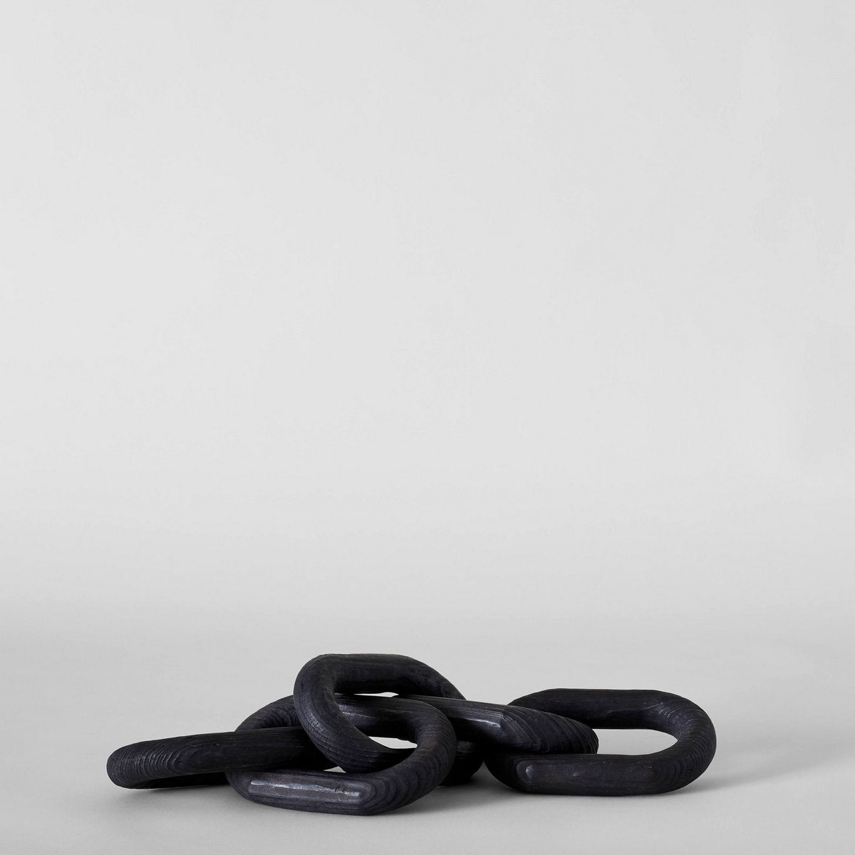 Black ceramic chain link sculpture on a minimalist white background