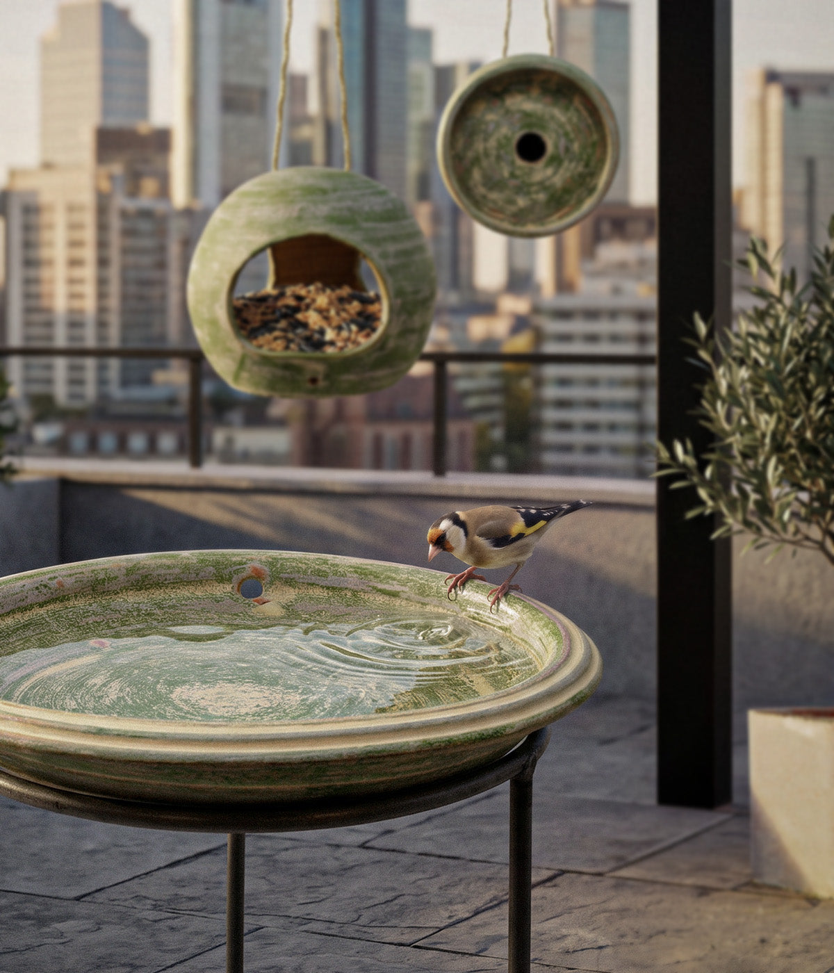 Garden Sage terracotta bird bath filled with water on a wrought iron stand, with a bird at the rim and coordinating bird feeder and birdhouse behind