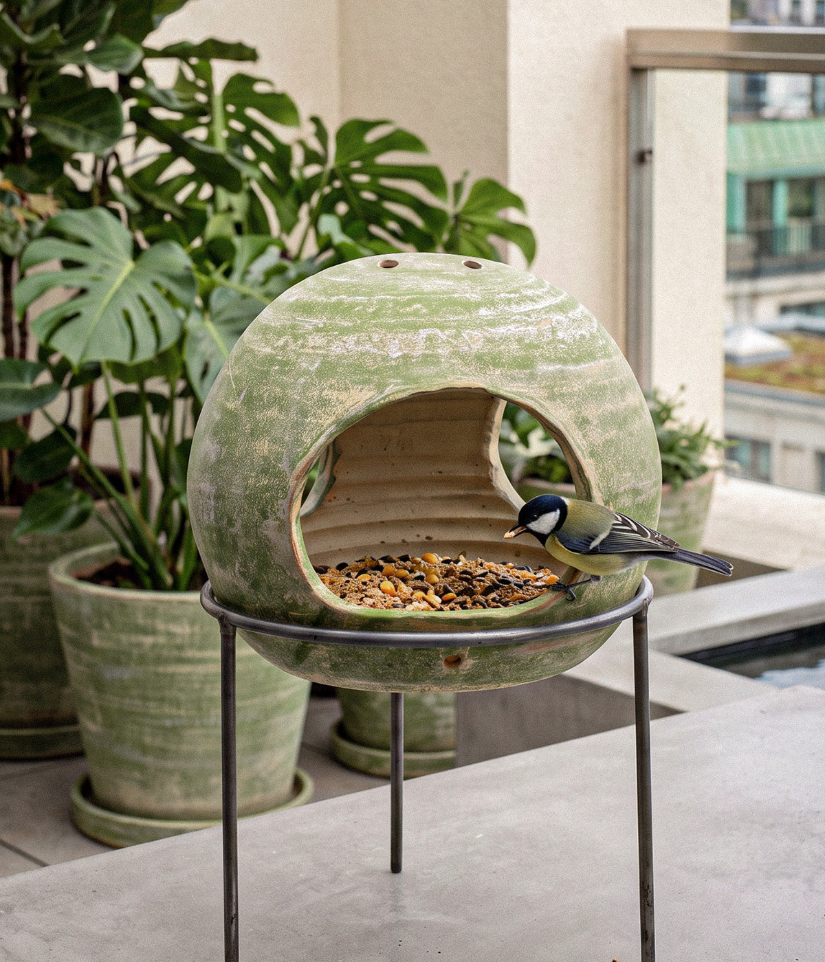Garden Sage terracotta bird feeder filled with seed on a wrought iron stand, with a small bird perched at the front opening