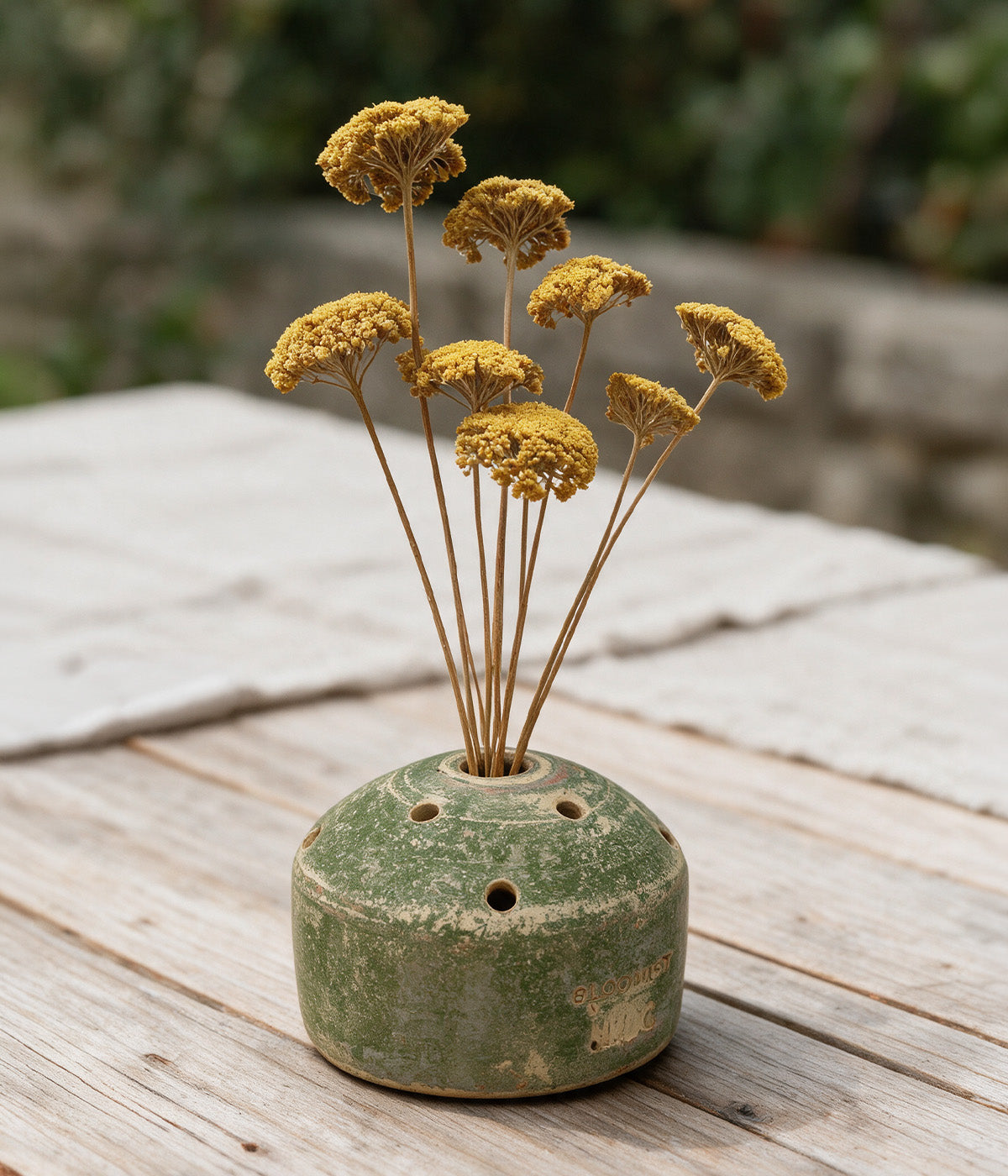 Garden Sage terracotta flower frog vase holding a loose arrangement of dried yellow flower stems on a wooden table