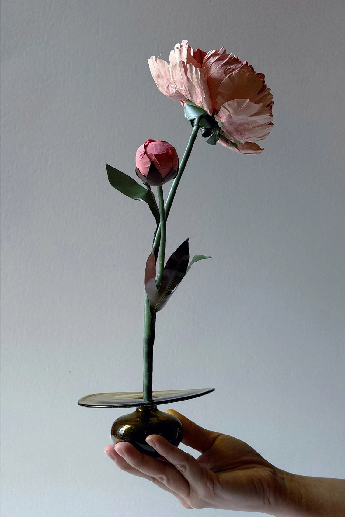 Hand holding a beeswax paper Chinese peony flower in a glass base