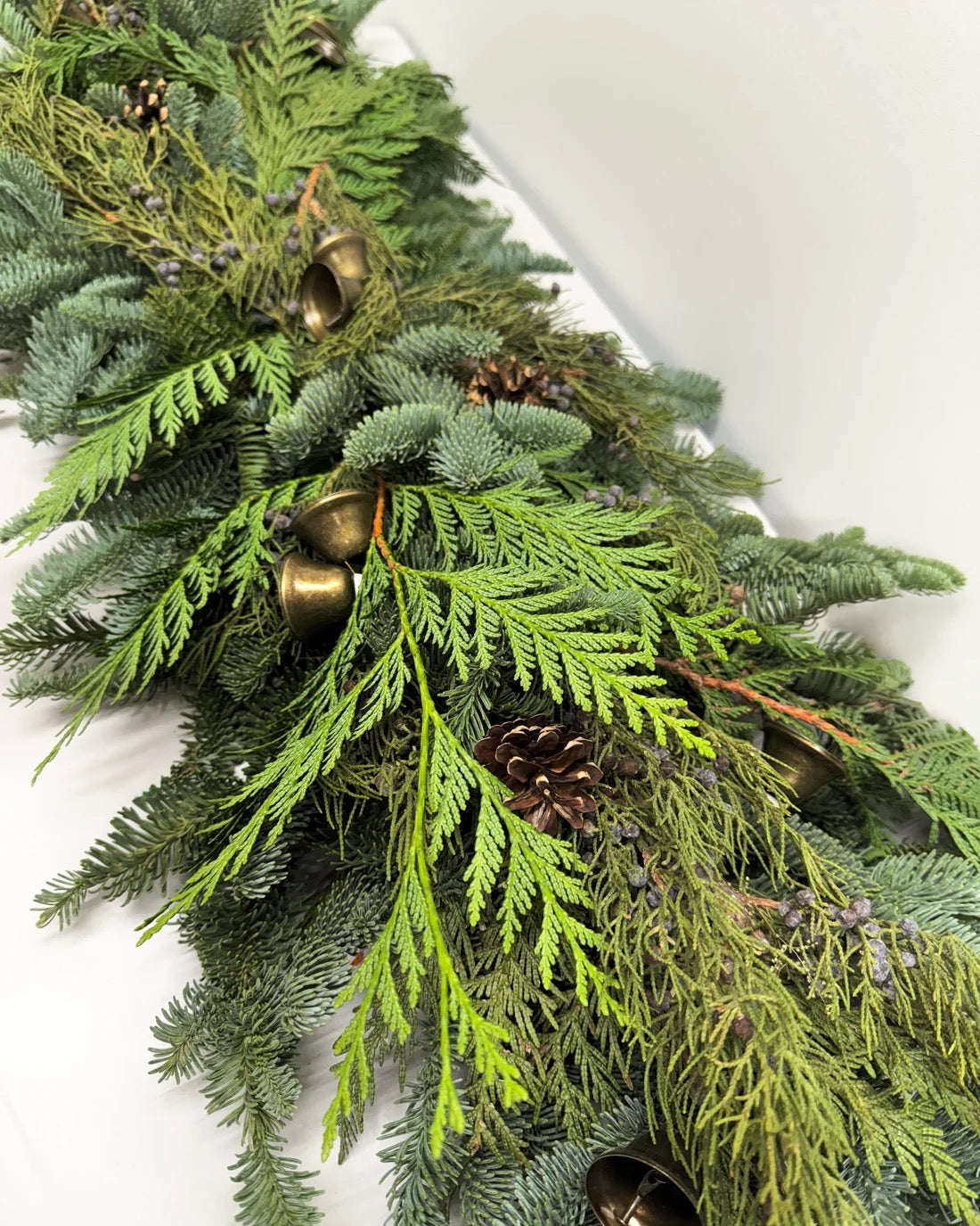 Close-up of Clara juniper garland with cedar, blue juniper berries, lodgepole pine cone, and antique-style bells
