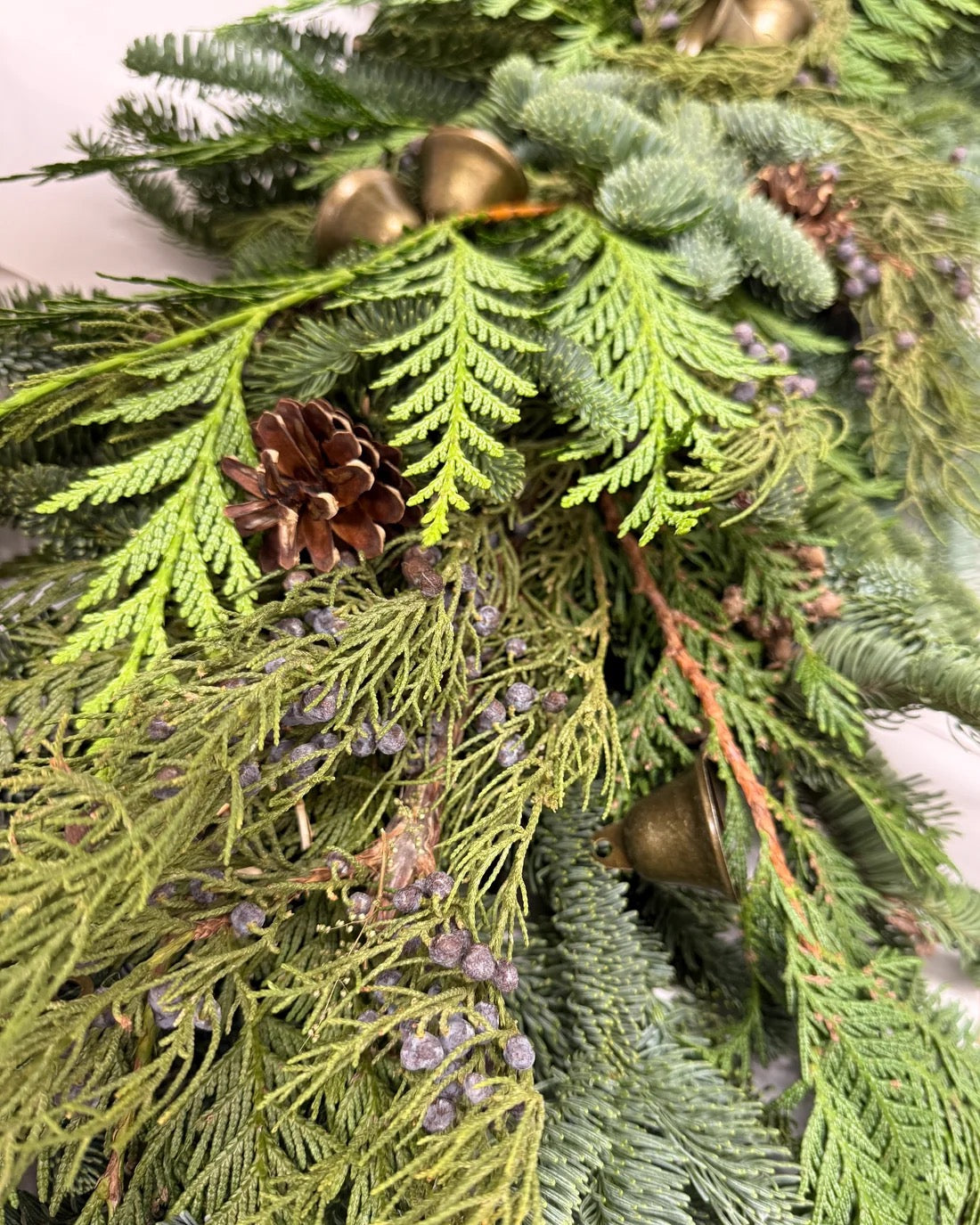 Close-up of fresh juniper garland with layered evergreens, blue berries, pine cones, and antique-style bells