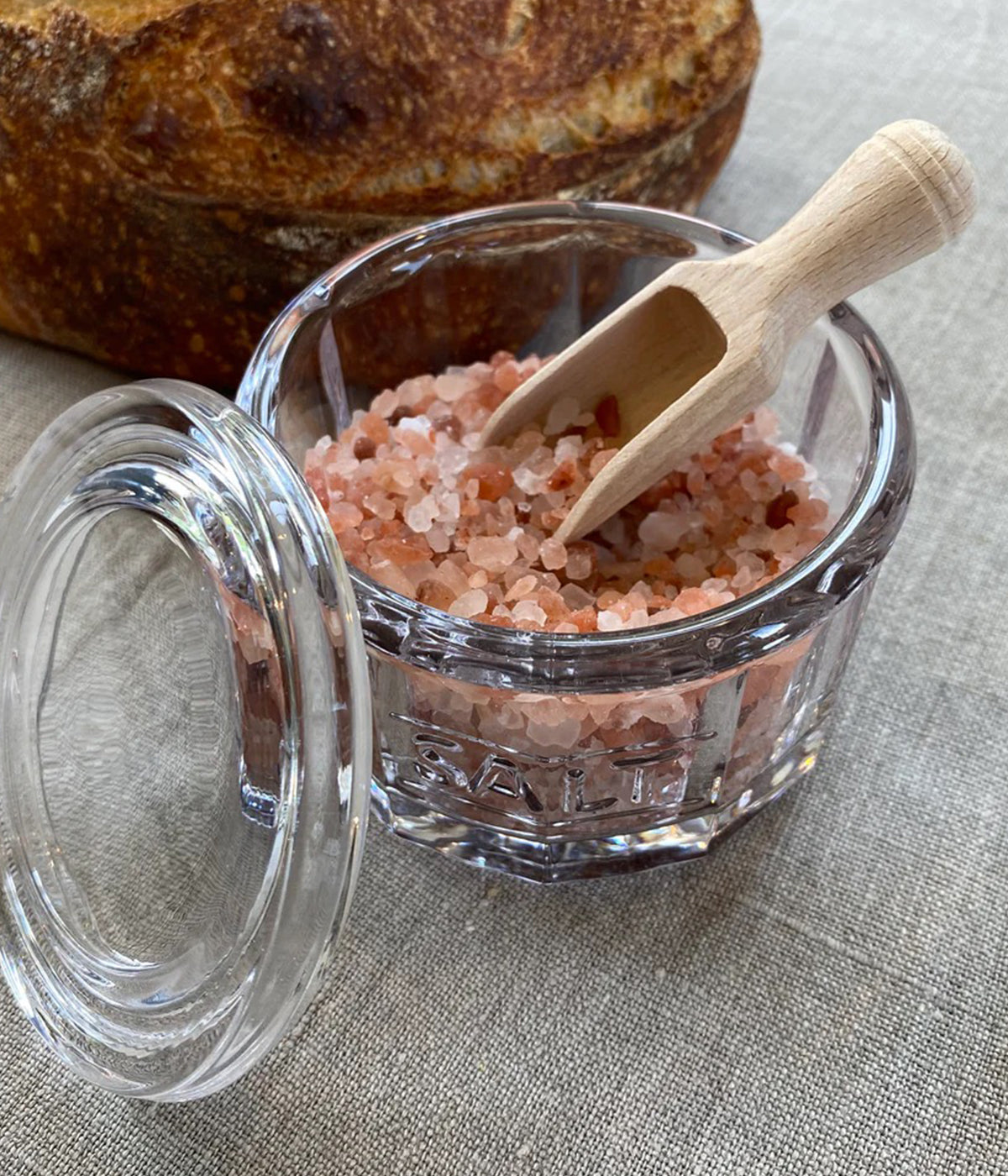 Clear glass salt jar with lid and wooden scoop for everyday kitchen use