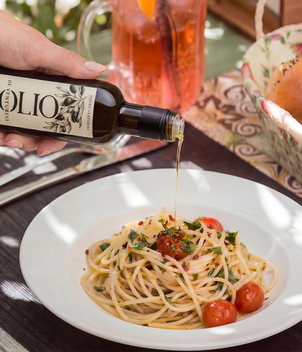 Hand pouring olive oil over pasta with herbs and cherry tomatoes