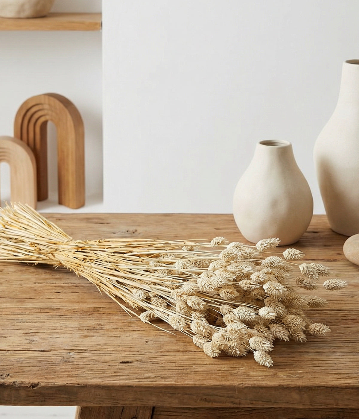 Whitewashed phalaris displayed on rustic wood table with neutral ceramic vases and wooden arch