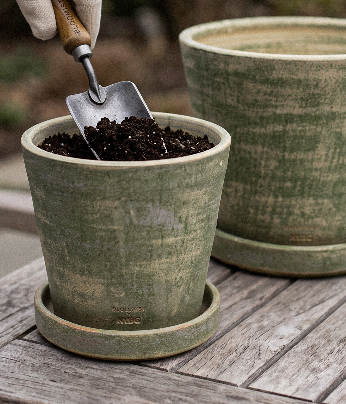 Garden trowel adding potting soil to a Garden Sage terra cotta planter with a larger matching planter behind it