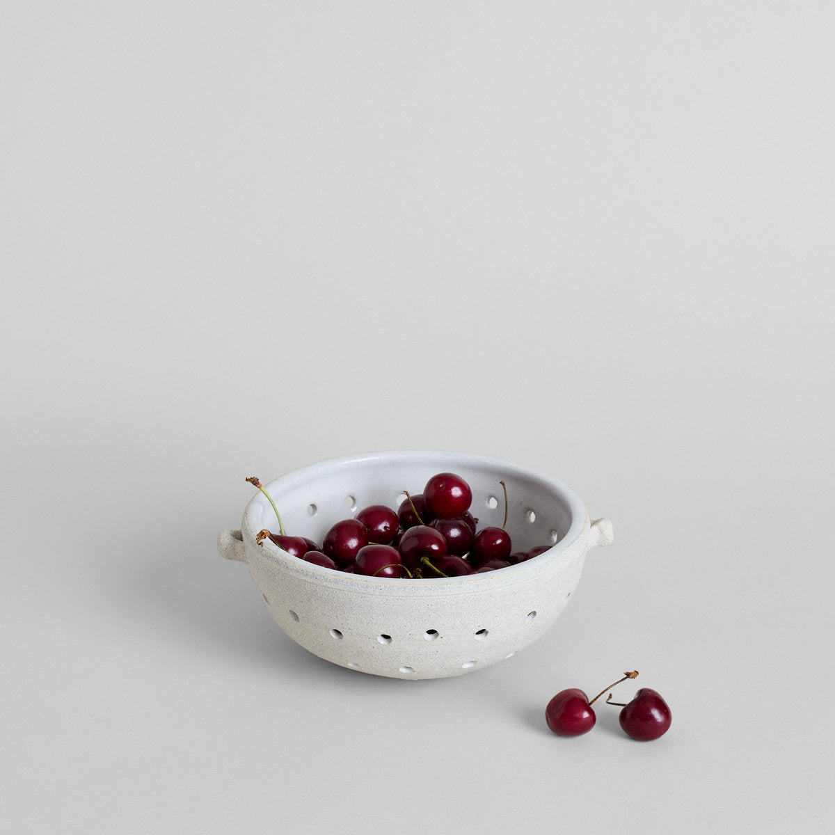 Hand-thrown ceramic berry colander with natural clay exterior and side handles