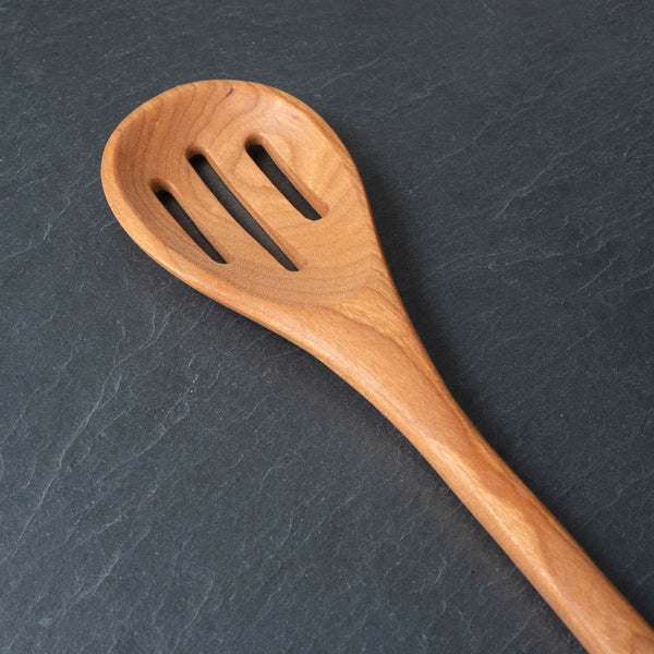 Slotted wooden spoon on a dark gray surface