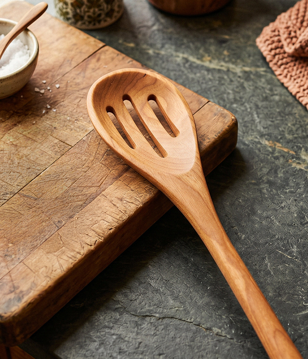 Wooden slotted spoon on a rustic wooden cutting board with a dark surface