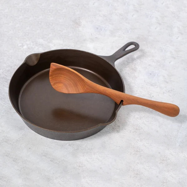 Black cast iron skillet with a handmade wooden resting corner spoon