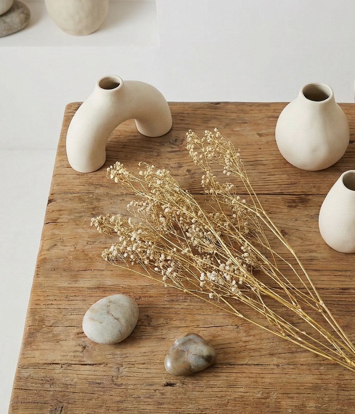 Dried baby's breath displayed on rustic wood table with sculptural ceramic vases