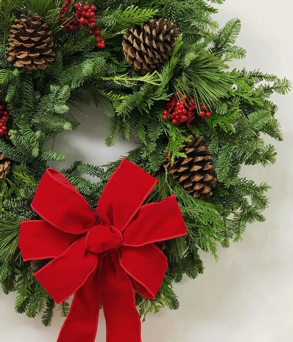 Close-up of Ruby wreath with red velvet bow, red berries, pine cones, and fresh evergreen branches
