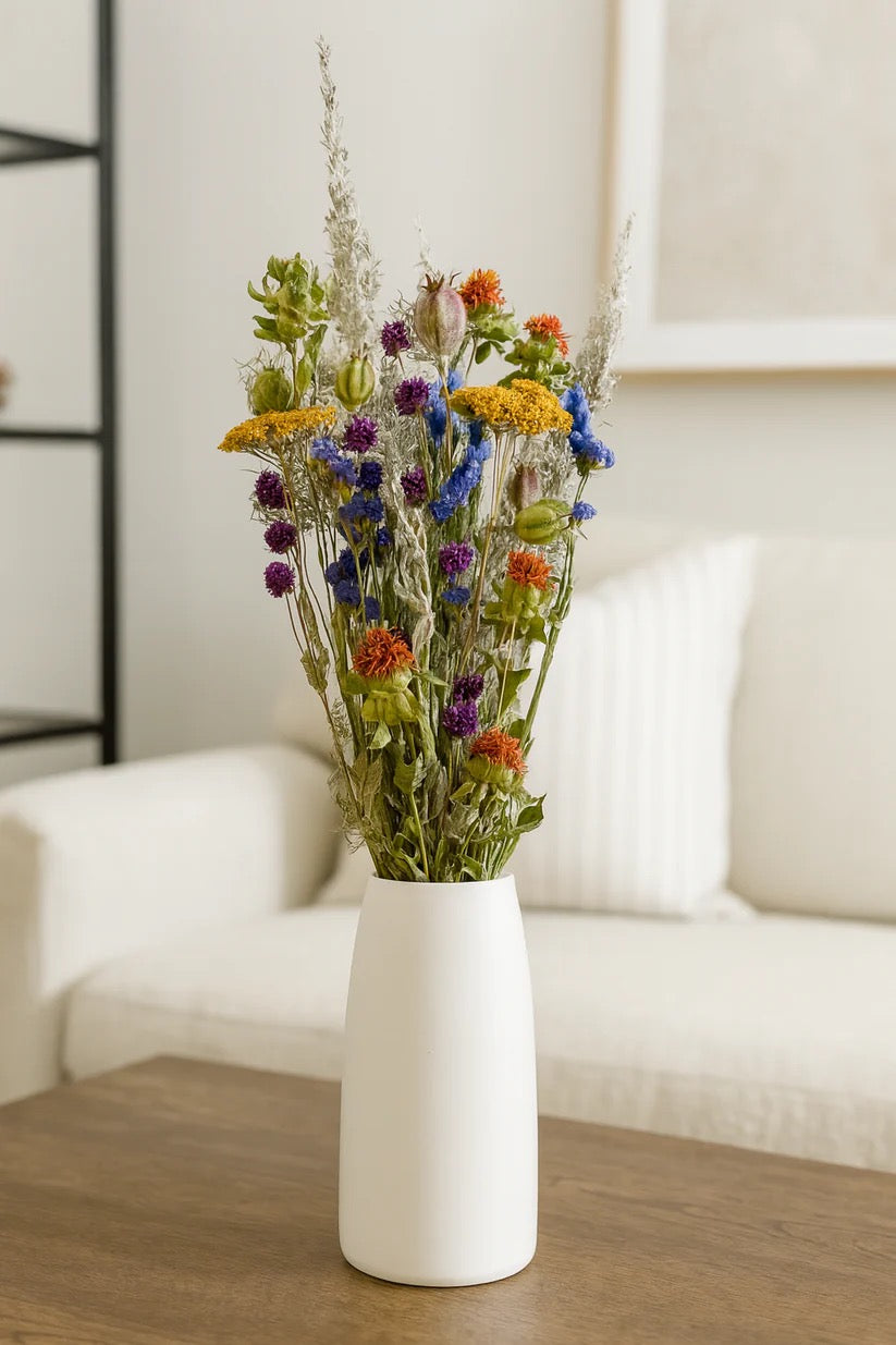Colorful dried flowers in white vase on neutral table with natural light