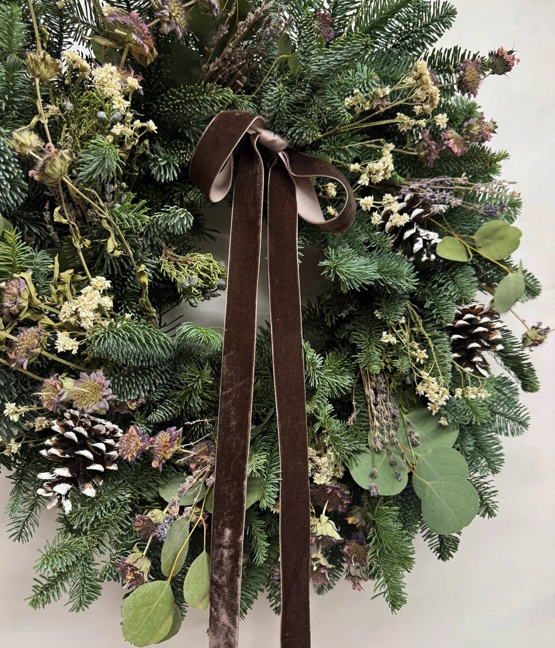 Close-up of Sylvie wreath with chocolate-brown velvet bow, lavender, pale blooms, eucalyptus, and fresh evergreens

