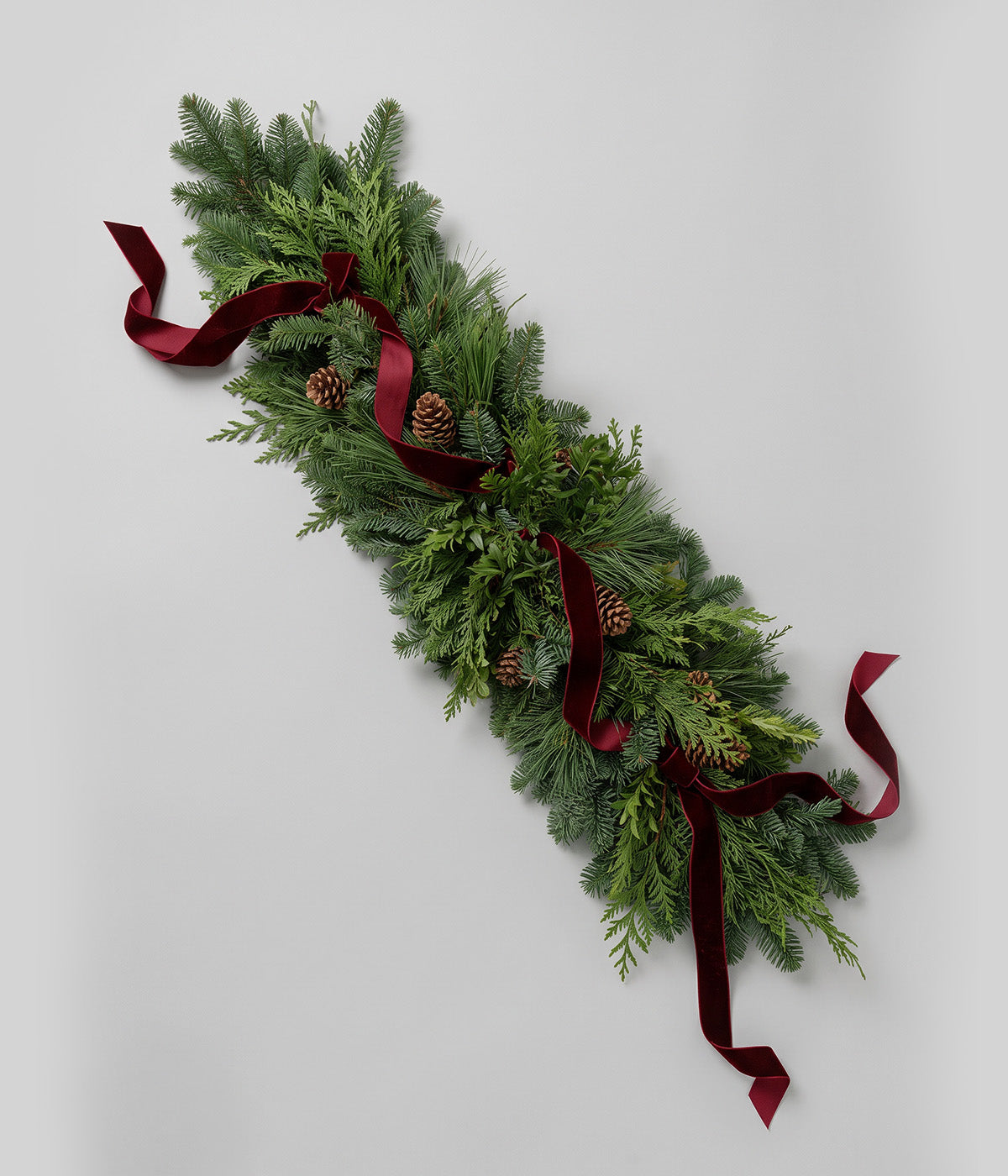 Coordinating fresh evergreen wreath with pine cones and burgundy velvet ribbon
