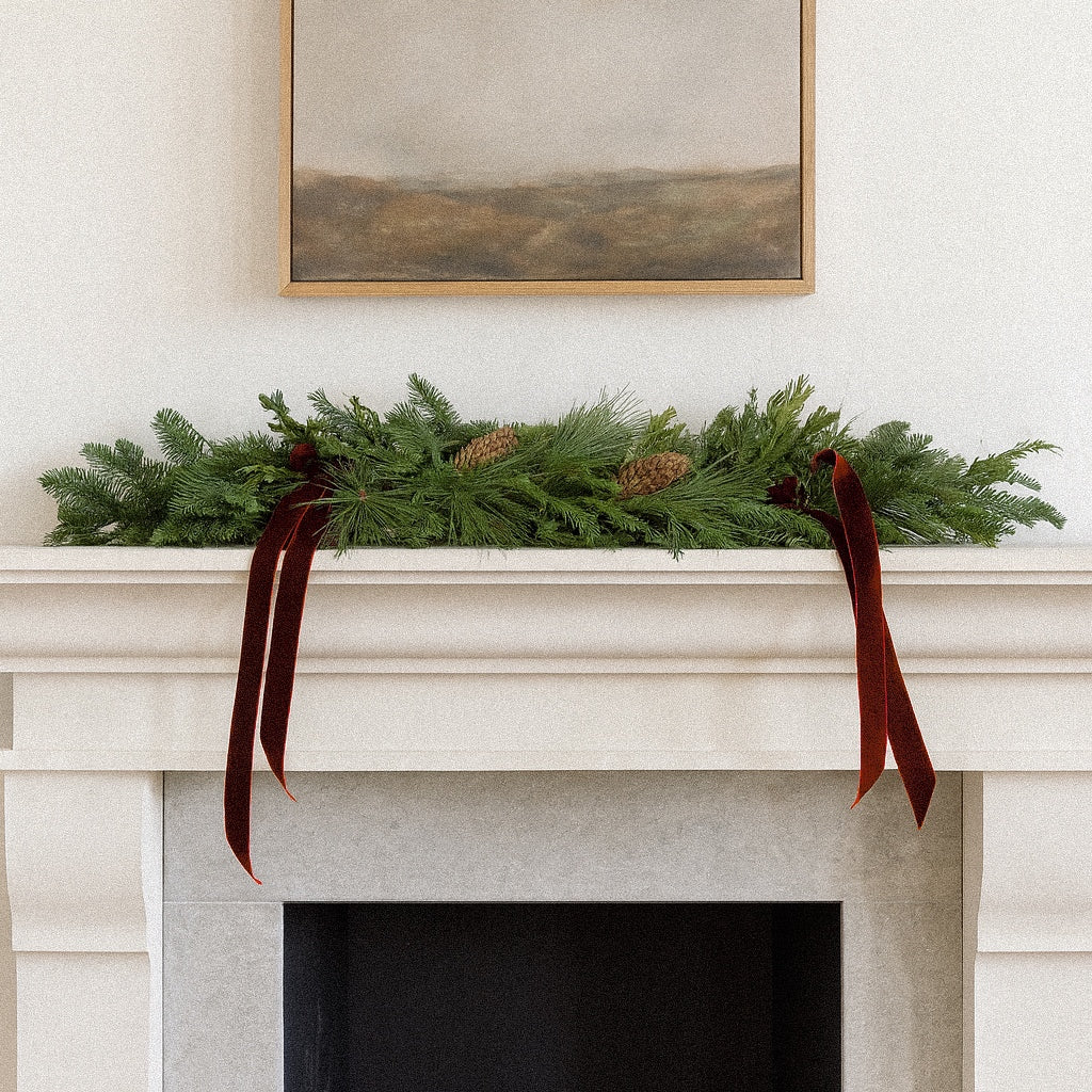 Vivienne Christmas mantel garland with fresh evergreens, spruce pine cones, and burgundy velvet across a white mantel
