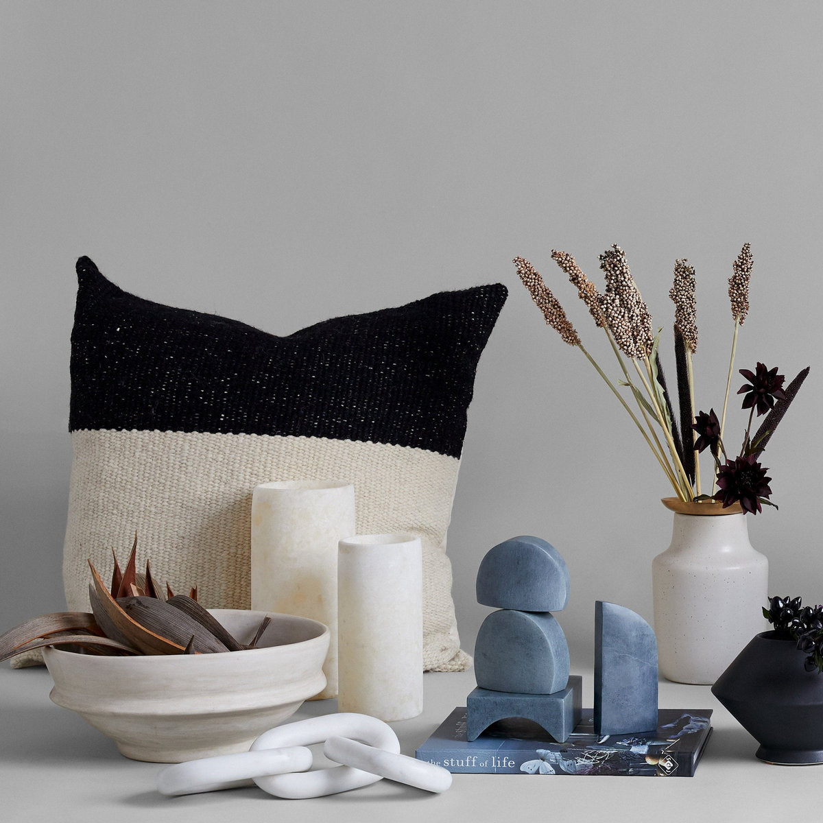 Dried palm paddles in white ceramic bowl on shelf with neutral home decor and textiles