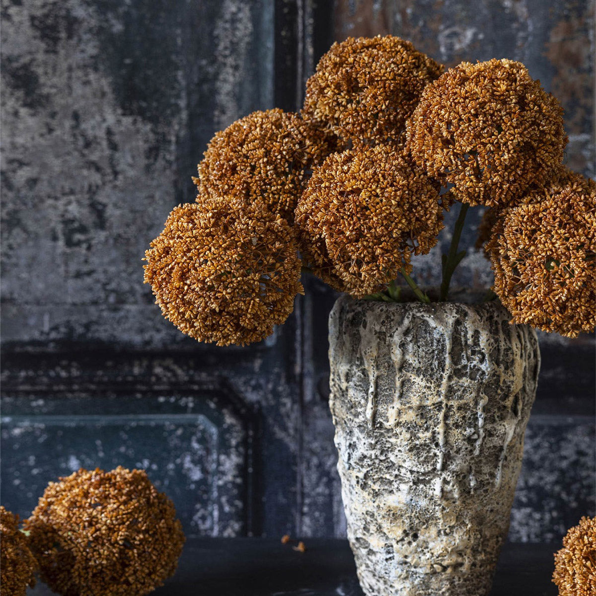 Artificial botanical stem with umber bloom arranged with sculptural greenery