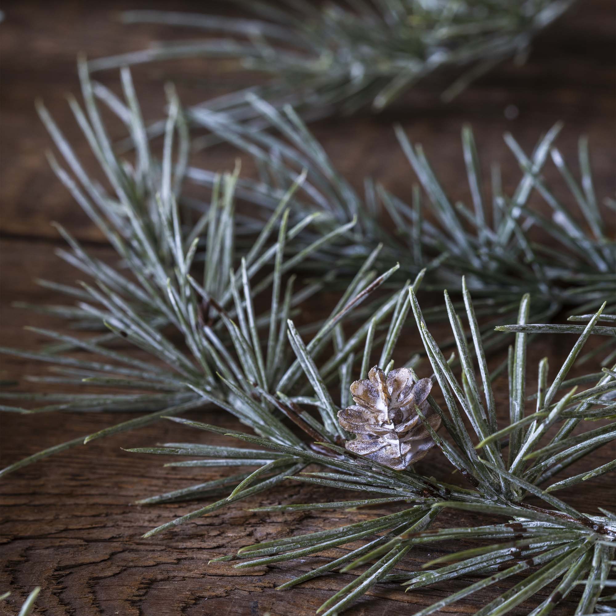 Artificial winter stem featuring cedar sprigs and pinecones on a neutral tabletop