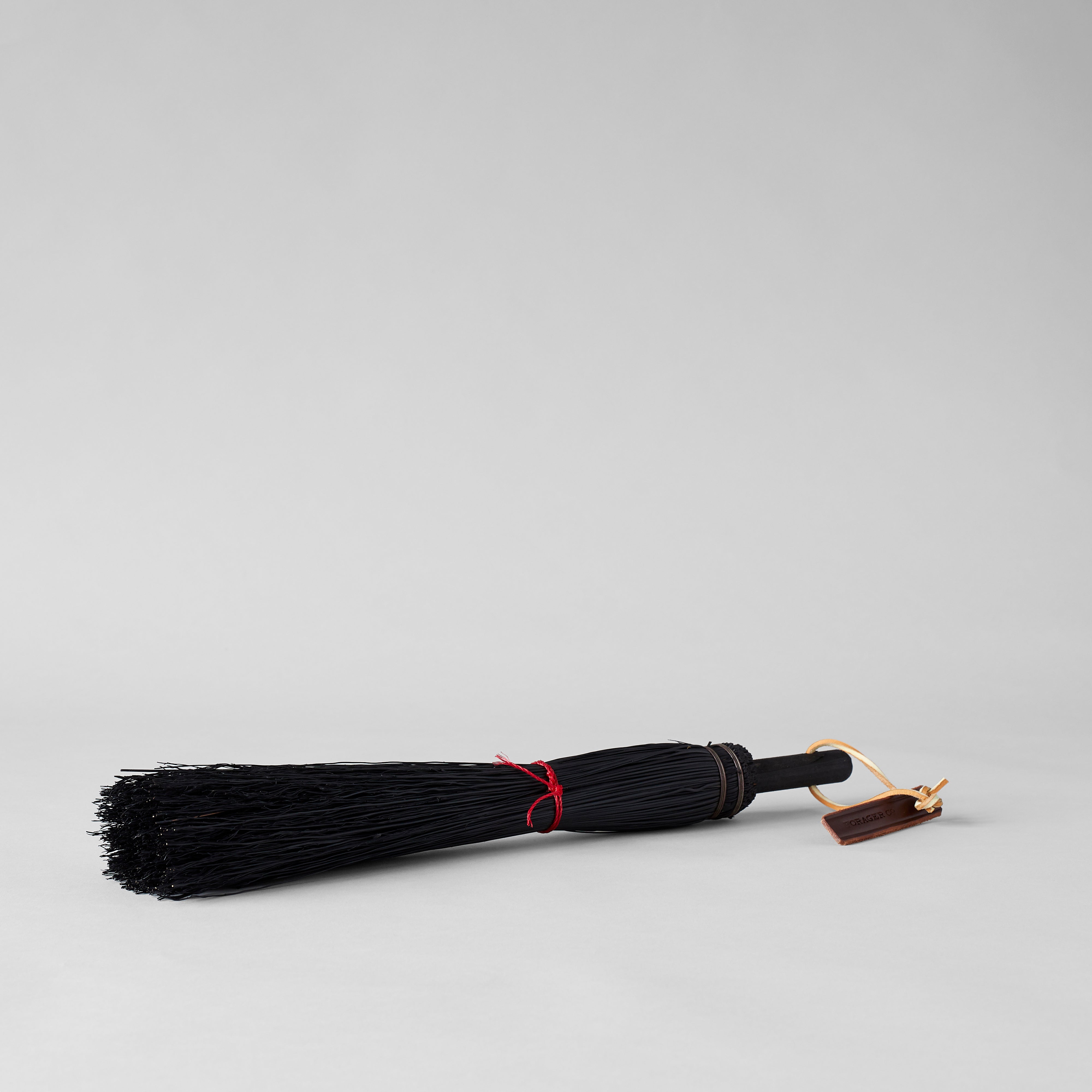 Rustic broom with black bristles, red cord, and leather loop